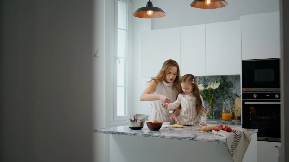 Jeune femme en tablier noir travaillant sur ordinateur portable dans cuisine professionnelle moderne, téléphone à l'oreille, prenant des notes